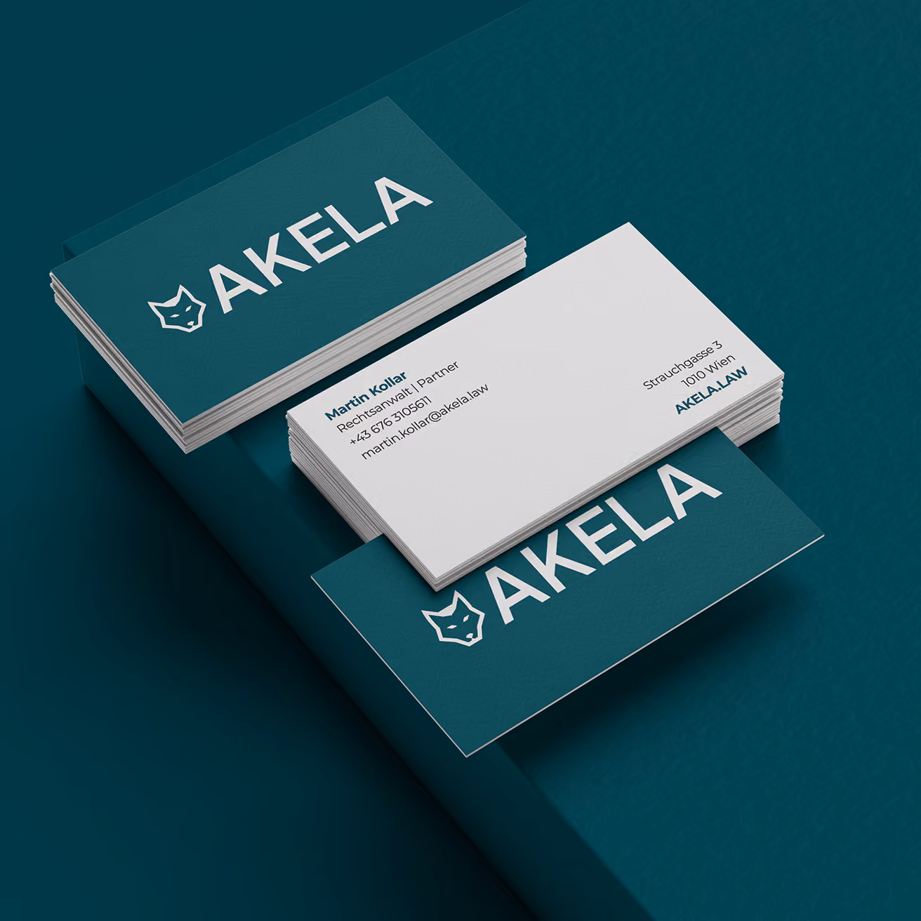 Stacked teal and white AKHELA business cards on a dark teal surface, featuring a fox logo, contact details, and a clean, professional design.