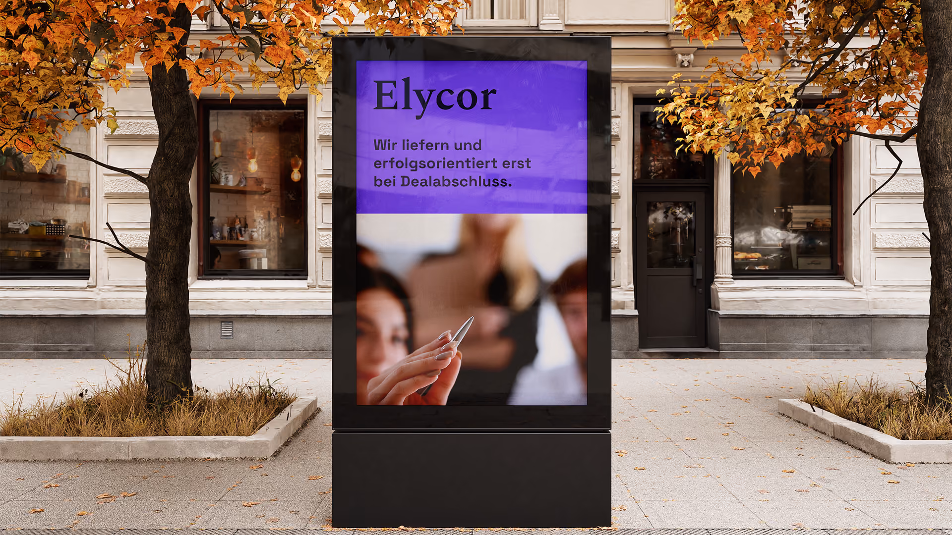 Digitale Werbetafel vor einem Altbau im Herbst: „Elycor“ wirbt auf Deutsch für erfolgreiche Erstgespräche; unscharfe Beratungsszene, warme Farben.