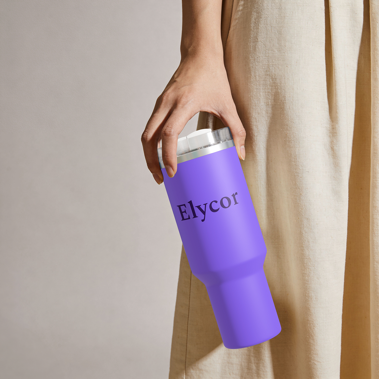 Eine Hand hält eine violette Elycor-Flasche mit silbernem Verschluss neben fließender, cremefarbener Kleidung vor neutralem Hintergrund – eine Szene, die eine ruhige, moderne Stimmung erzeugt.