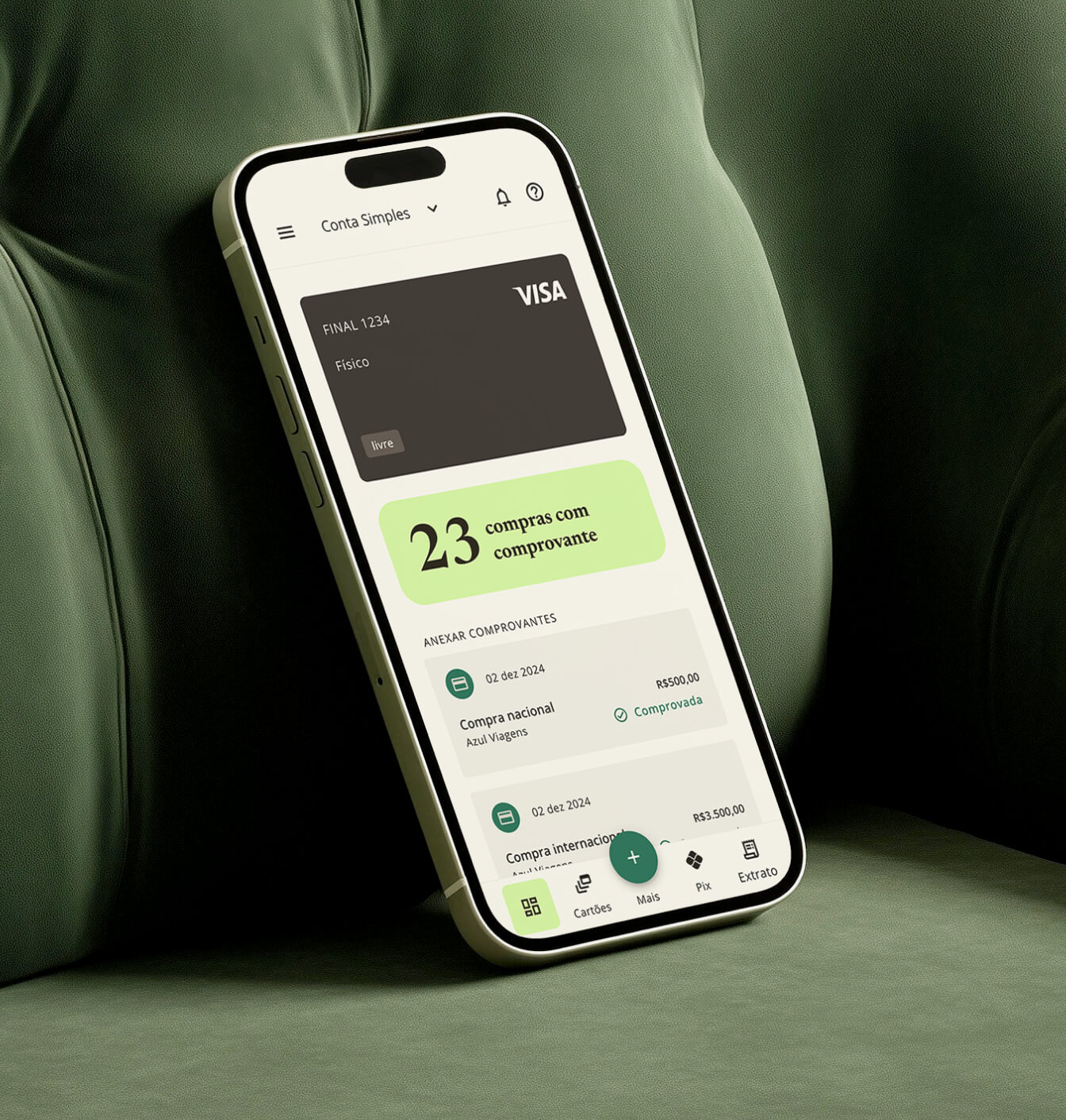 Smartphone em um sofá verde exibindo aplicativo bancário com cartão Visa, 23 compras com comprovante, e detalhes de compras nacionais e internacionais.