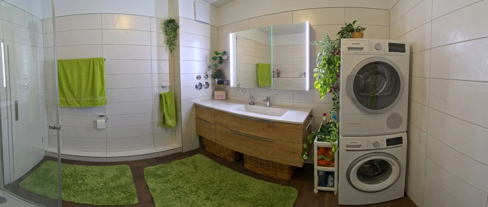 Modernes Badezimmer mit grünen Handtüchern, Teppichen, Holzmöbeln und gestapelter Waschmaschine und Trockner.