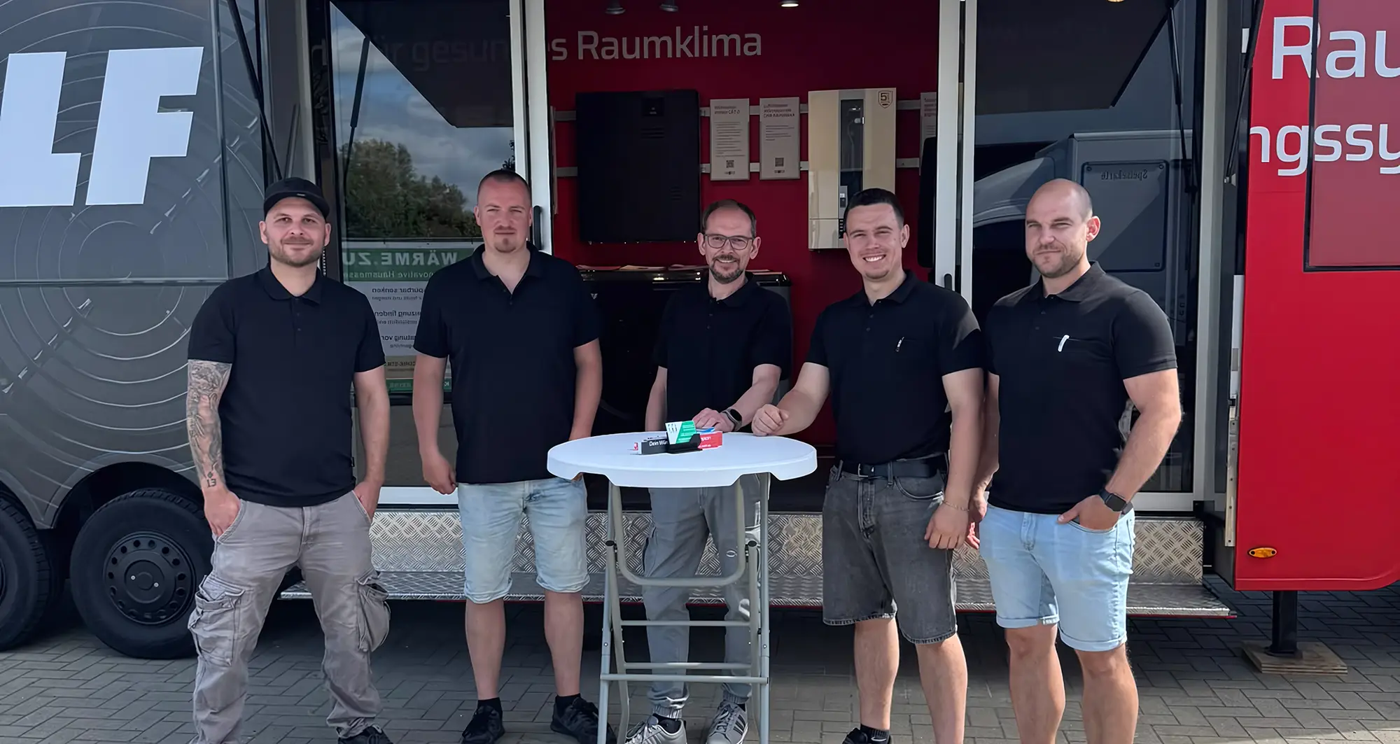 Acht Personen in Arbeitskleidung stehen vor einem weißen Firmenfahrzeug mit einer Werbetafel.