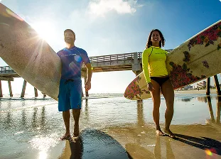 Two people walking up Jacksonville beach holding surfboards