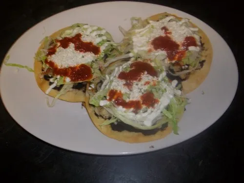 3 tostadas served on a plate with beans, lettuce, red sauce, sour cream and cheese.