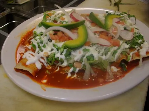enchiladas rojas, served on a plate with avocado, cheese, sour cream and onion.