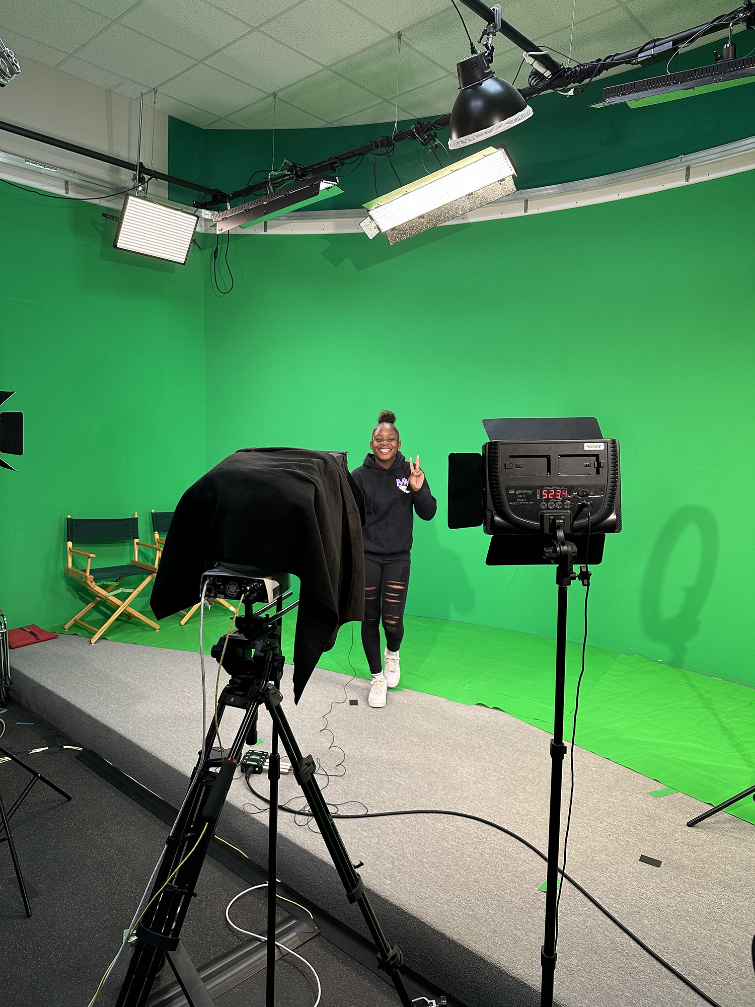 A young MVTV member poses in front of the camera, testing a green screen setup in the studio