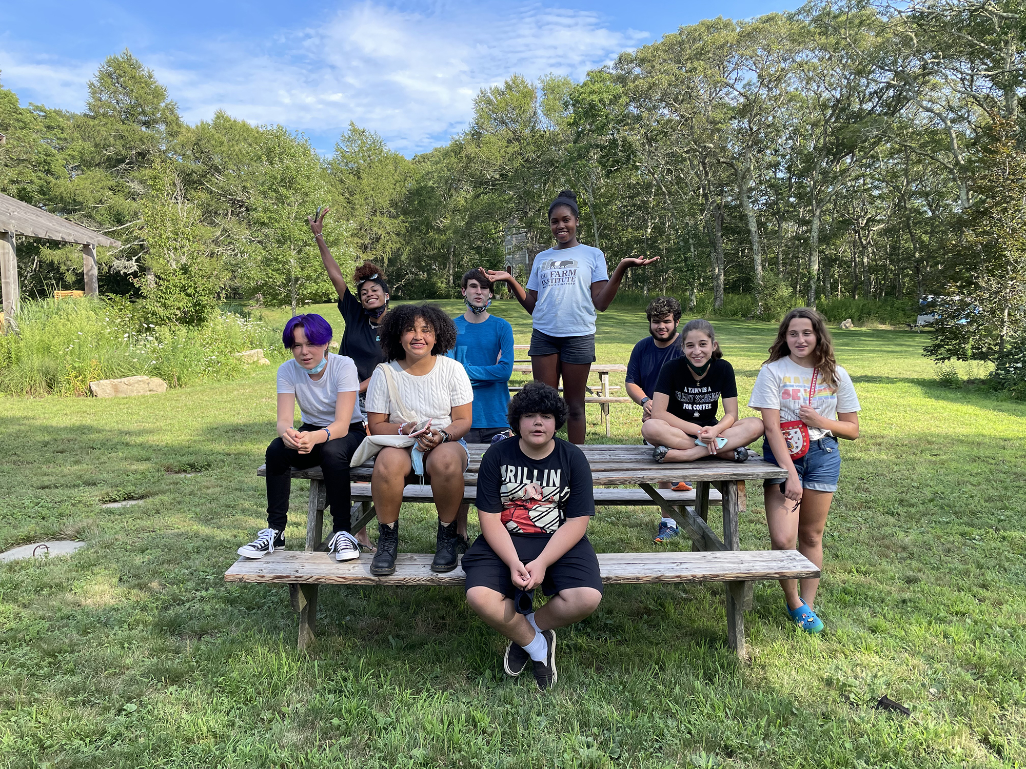 A group of MVTV camp students sit on benches outside on a sunny day and smile for the camera