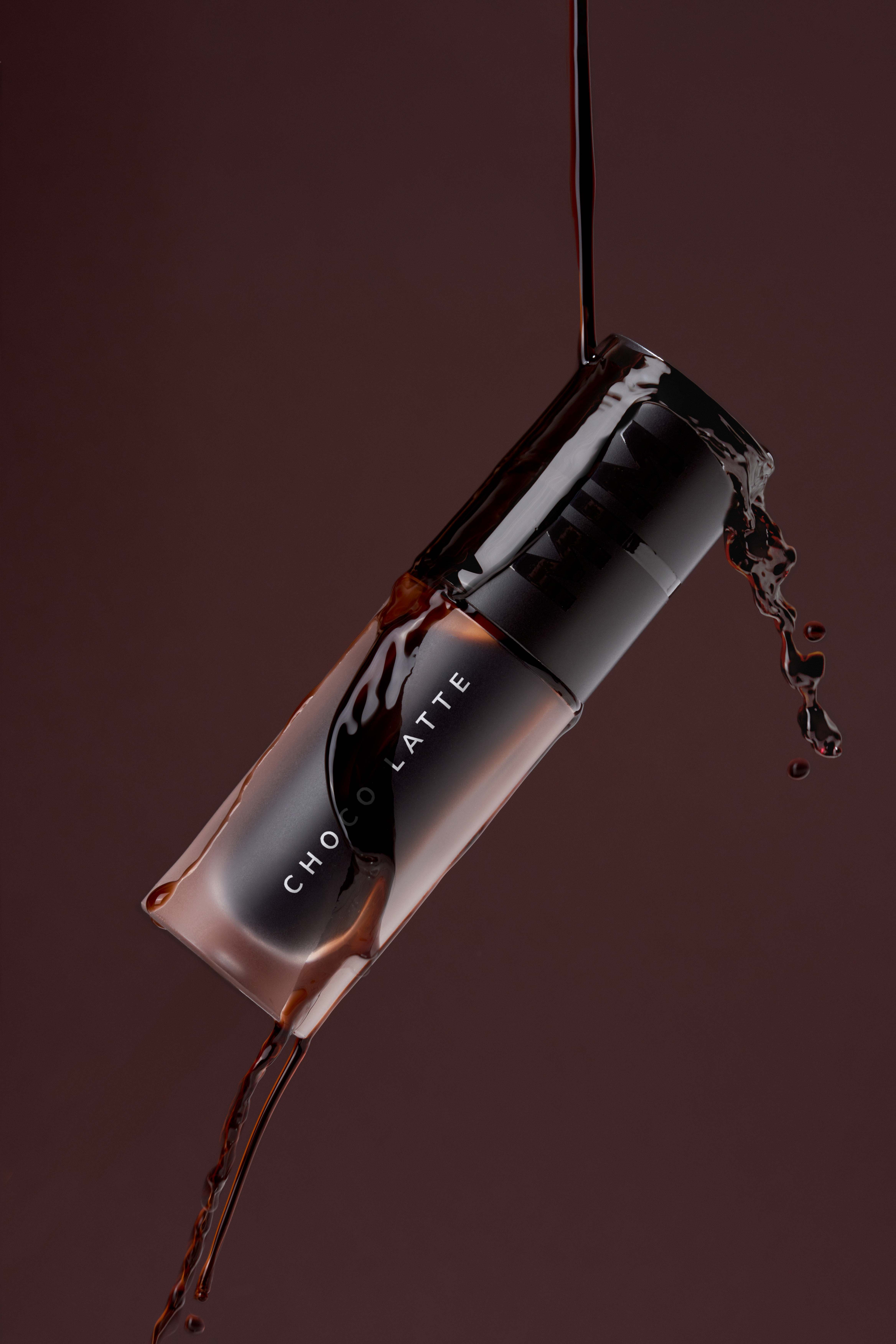 Product photography by Gooper with a dynamic splash effect: MIM Choco Latte lip gloss spilling over a rich brown background.