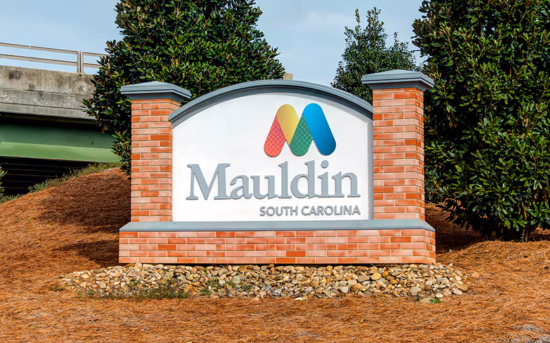 Entrance sign for Mauldin, South Carolina, made of brick with colorful M logo and greenery in the background.
