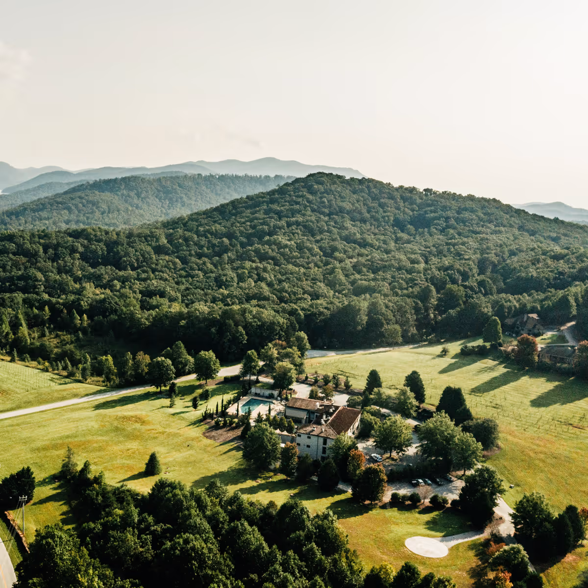 Aerial view of a large hotel in Travelers Rest South Carolina surrounded by green fields and dense forested mountains under a clear sky.