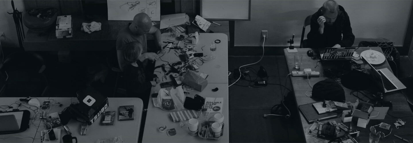 Overhead view of an adult and child assembling electronic components at a cluttered worktable, collaborating on a hands-on project.
