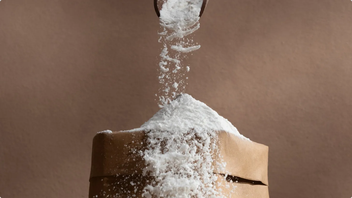Flour being scooped onto a paper bag against a brown backdrop