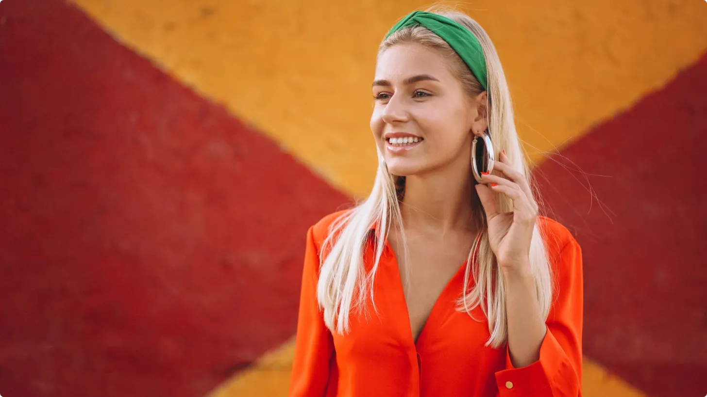 Young woman with a green headband smiling against a red and orange patterned wall