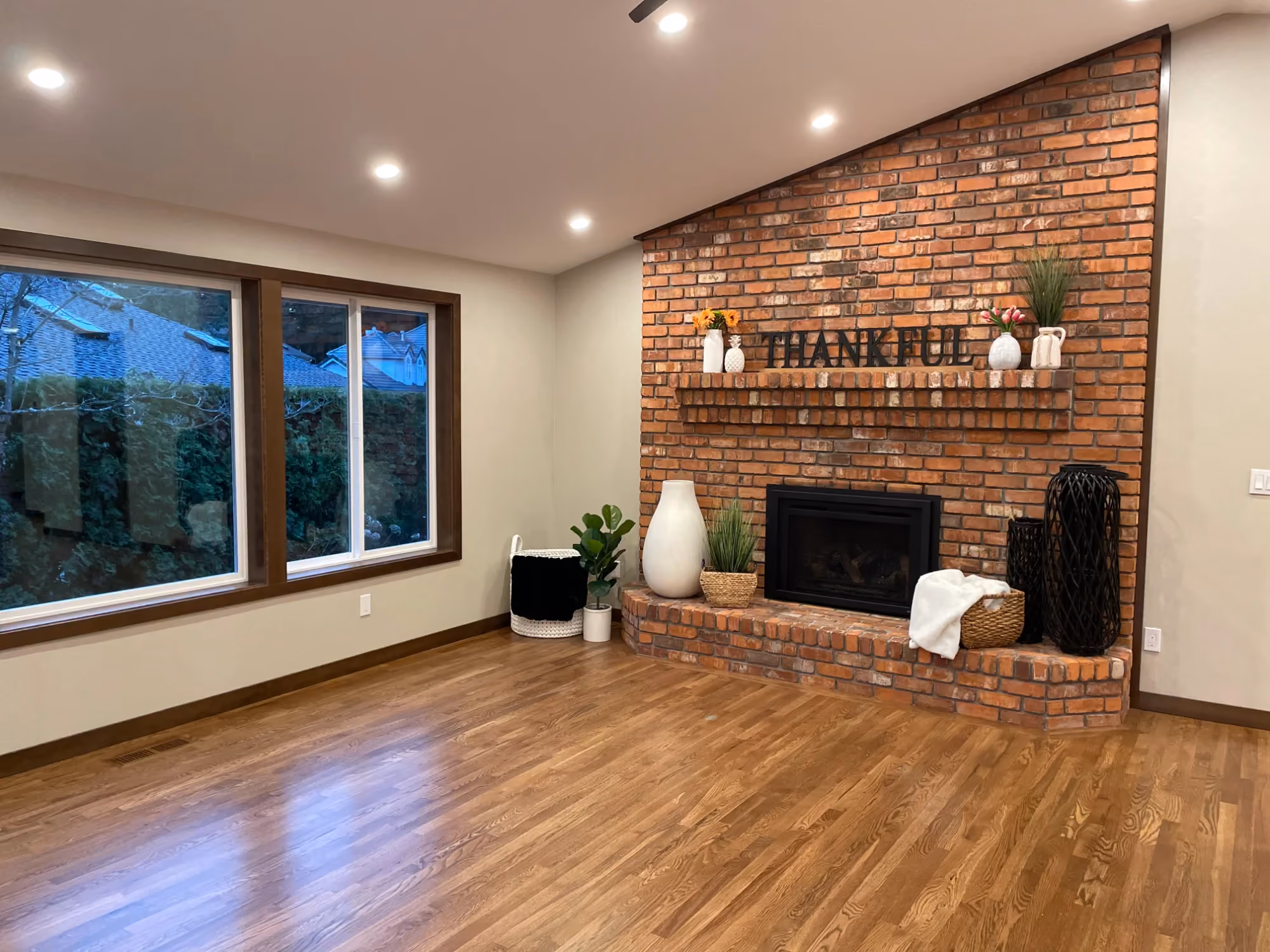 Living room with brick fireplace, hardwood floors, and large windows