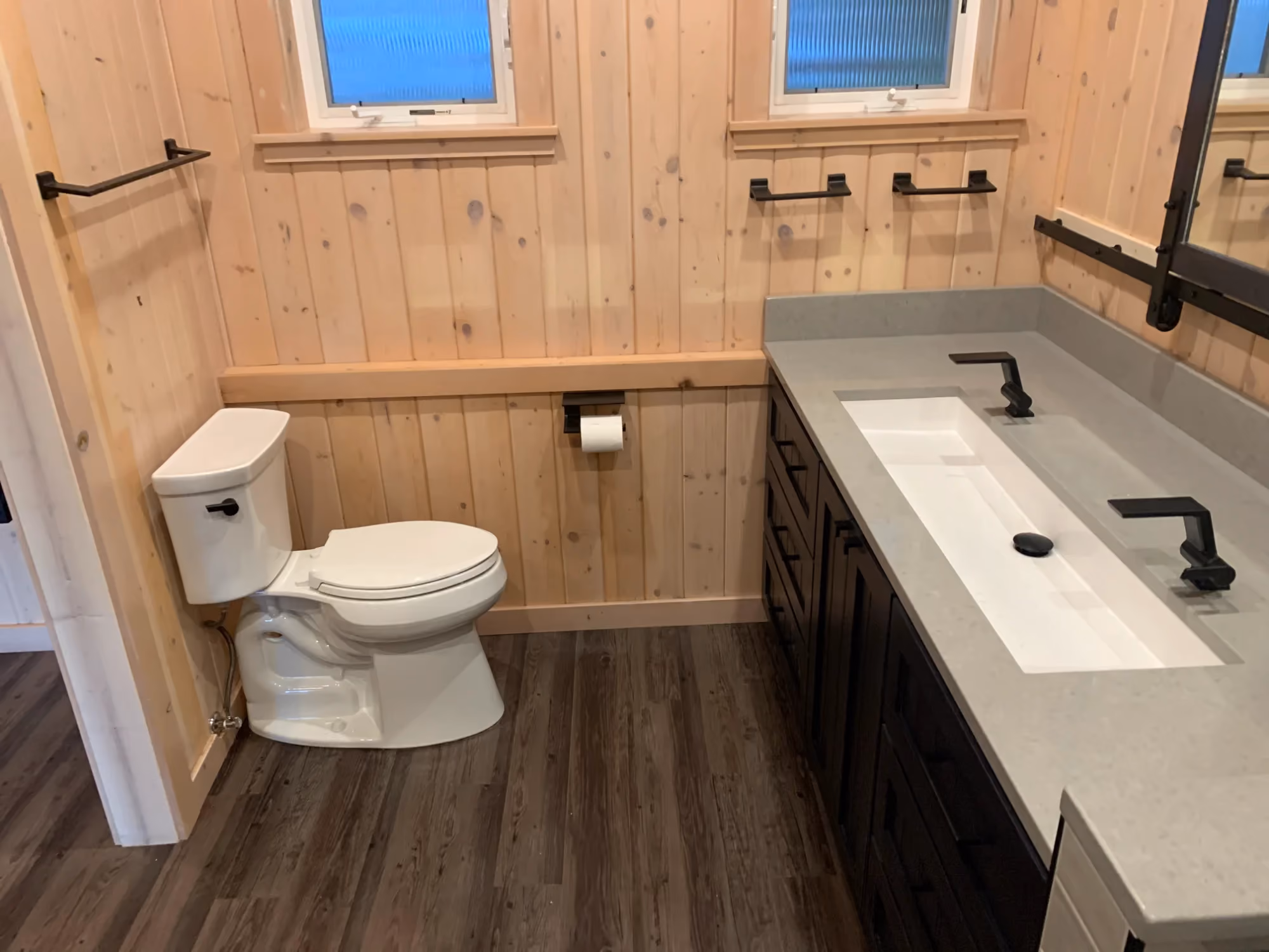 Rustic bathroom with wood walls, toilet, and double-sink vanity