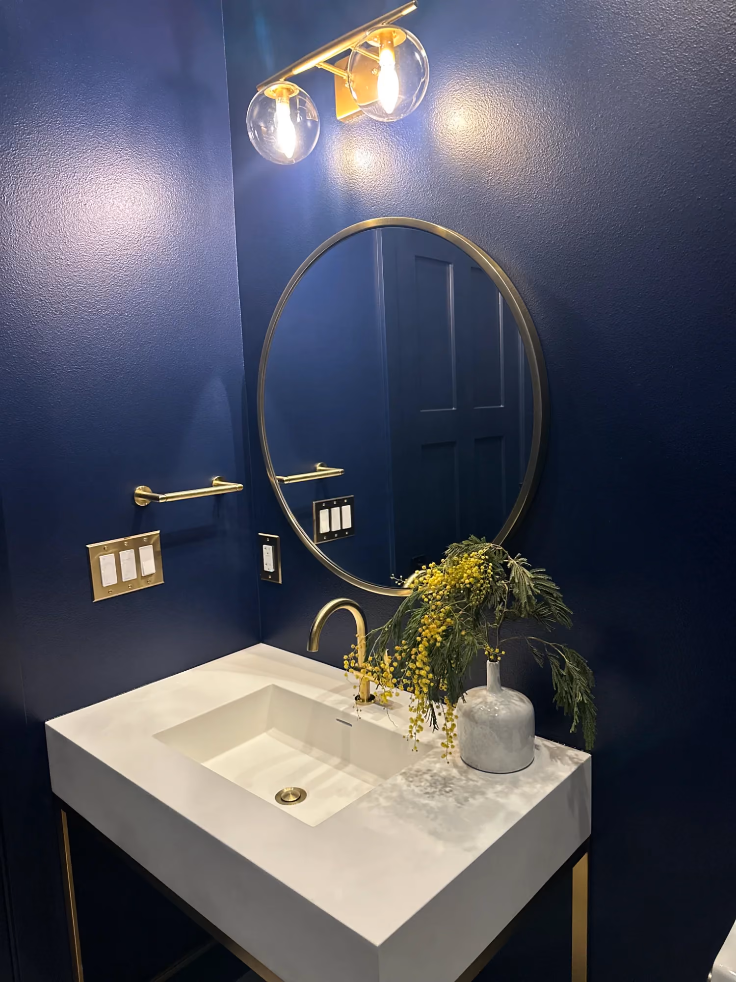 Navy bathroom vanity with round mirror and gold fixtures