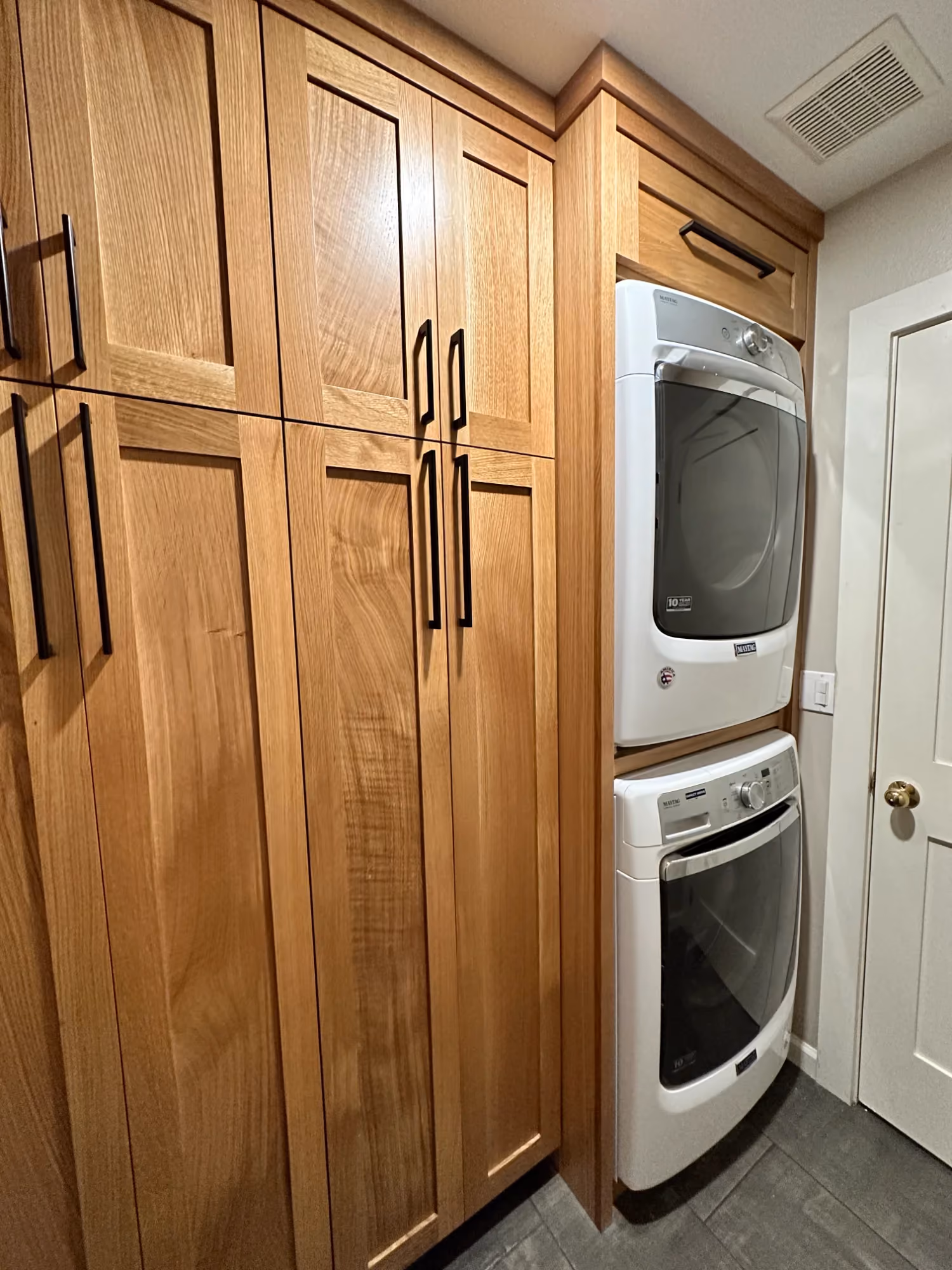 Laundry closet with washer and dryer beside wood cabinetry