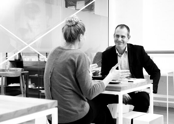 Man and woman sitting at a table engaged in a conversation in a modern, bright room.