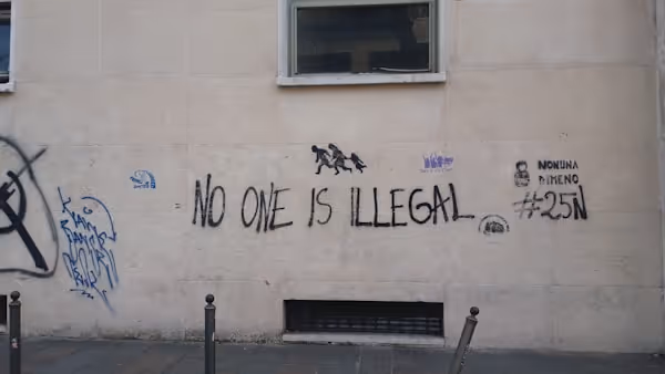 Graffiti on a wall reads "No one is illegal" in all caps.