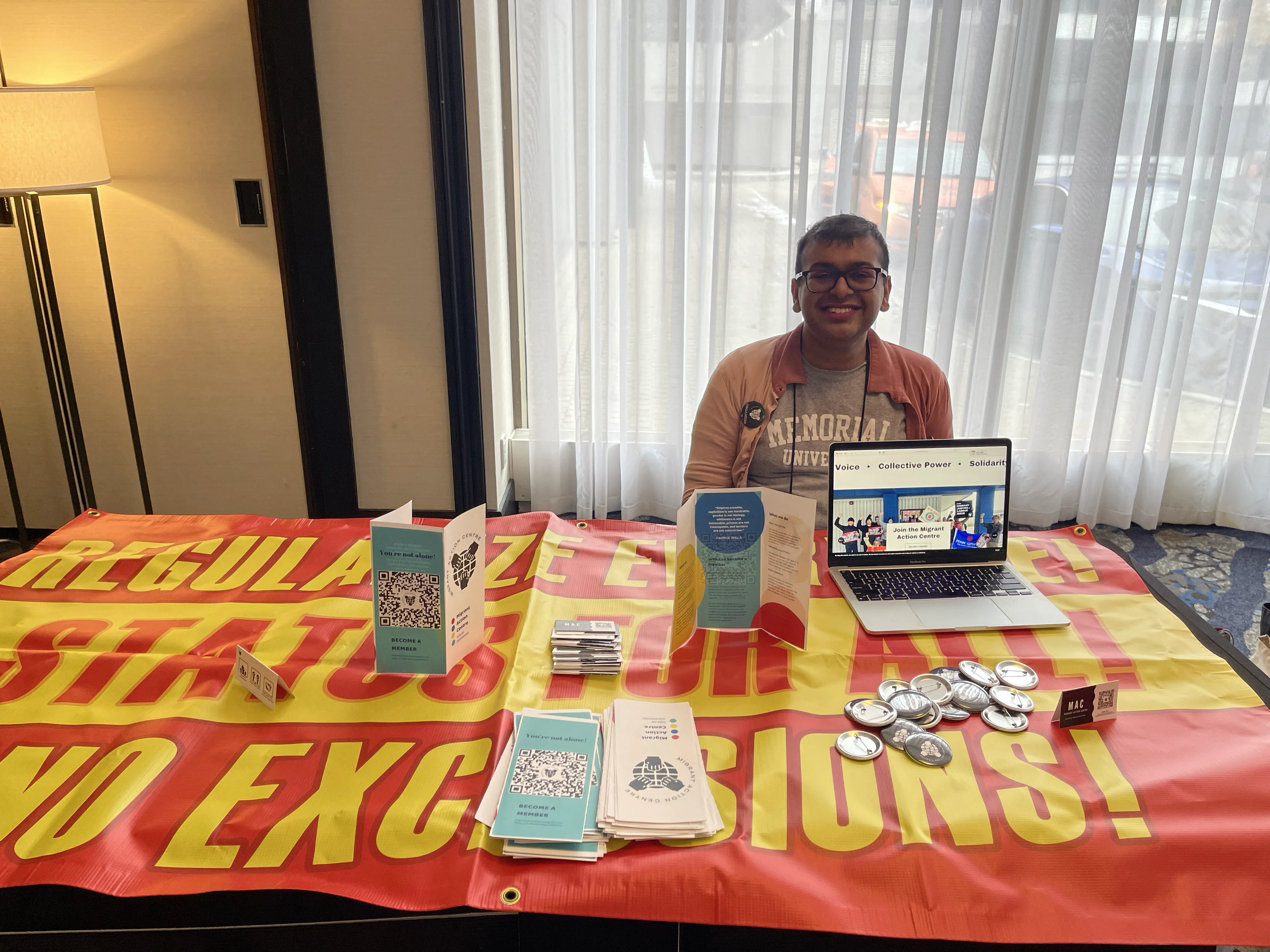 A MAC organizer at an outreach table with a laptop, campaign materials, and a status for all banner.