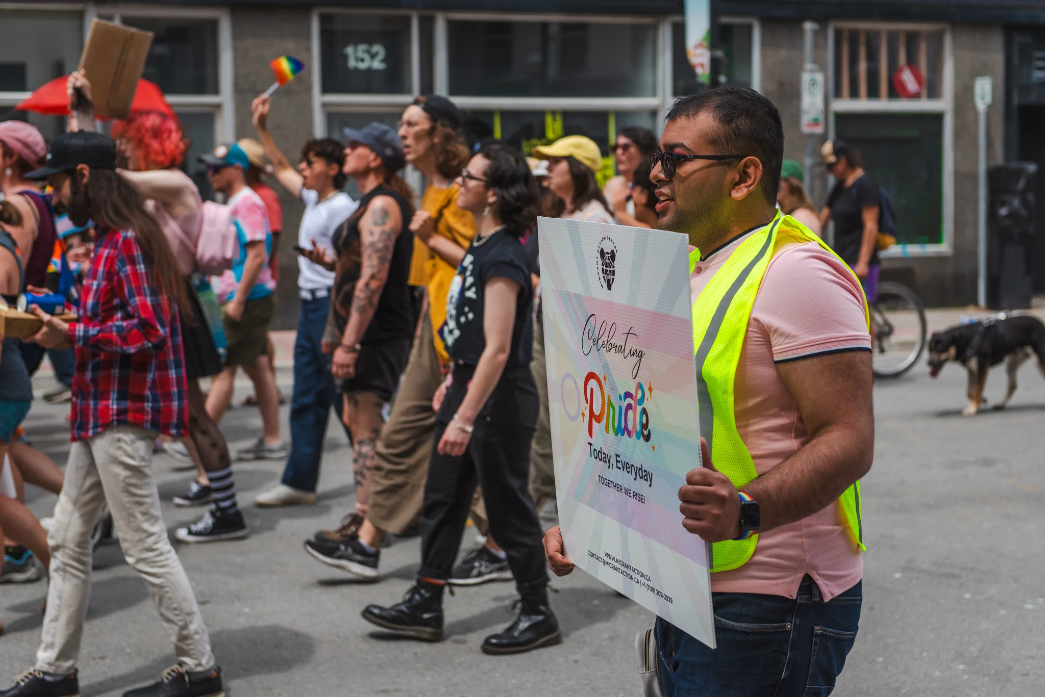 A MAC organizer marches in a pride event, holding a sign reading "Celebrating Pride
Today, Everyday
Together We Rise!"
There is a crowd of marchers in the background.