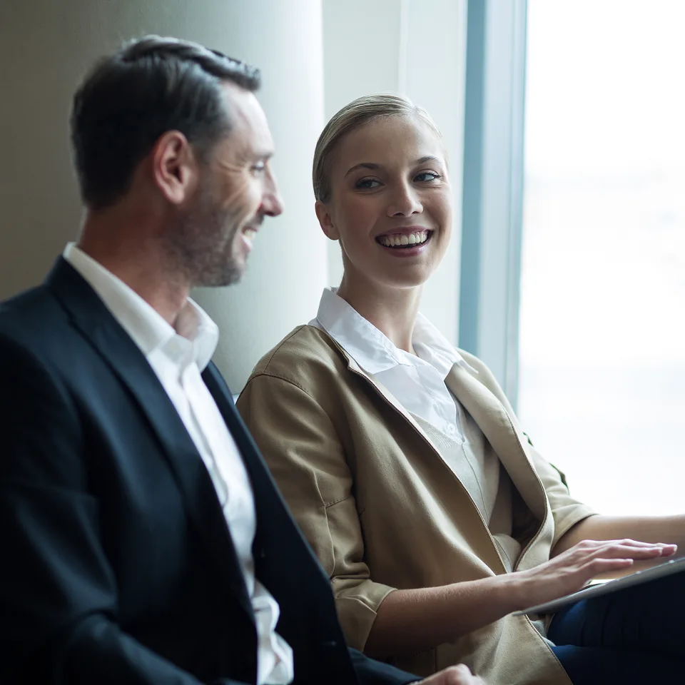 Smiling businesswoman interacting with a male colleague by a window in a modern office.