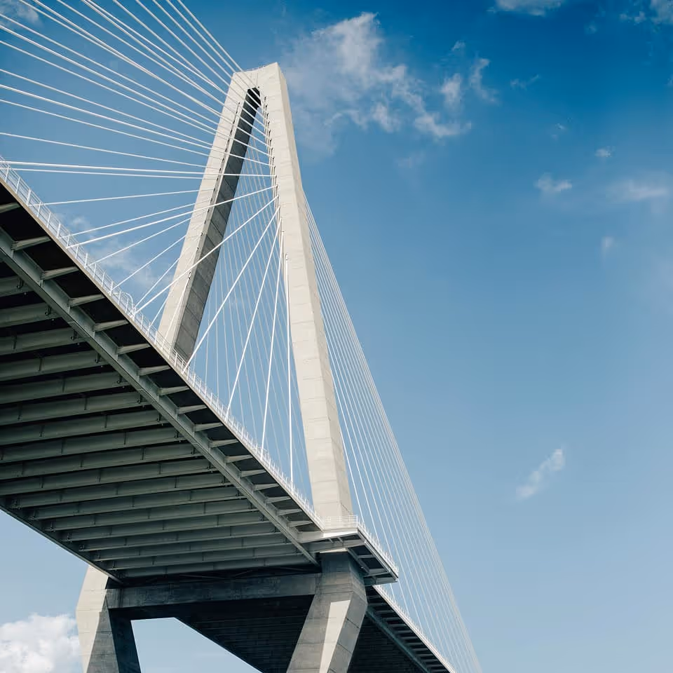 Low angle view of a cable-stayed bridge with a tall concrete tower against a blue sky.
