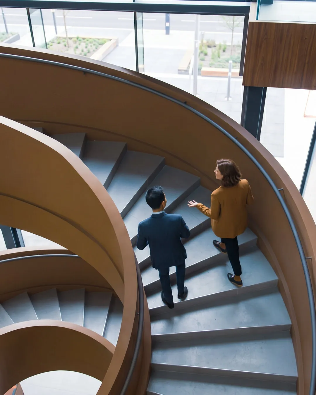 Two businesspeople walking down a curved indoor staircase having a discussion.
