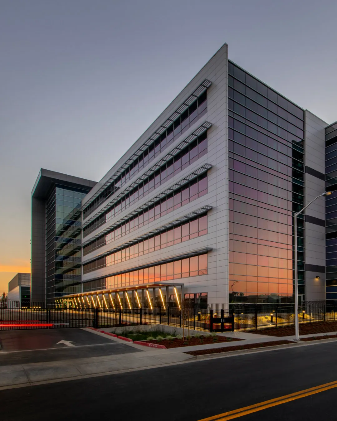 Modern commercial building at sunset with glass windows reflecting the sky and lit entrance area.
