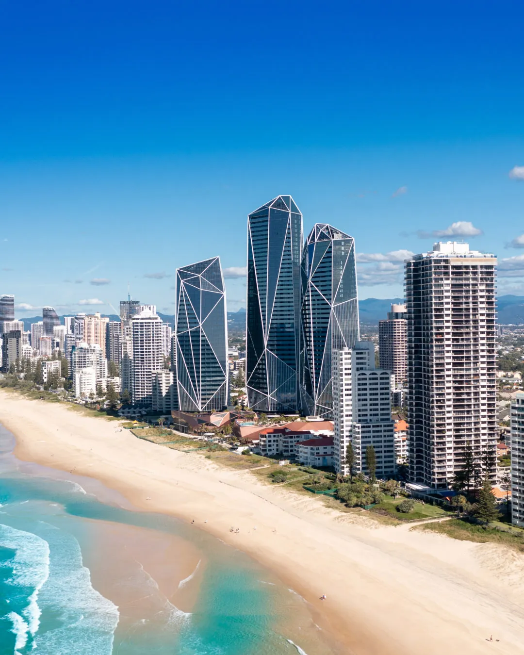 Modern skyscrapers and high-rise buildings along a wide sandy beach with ocean waves.