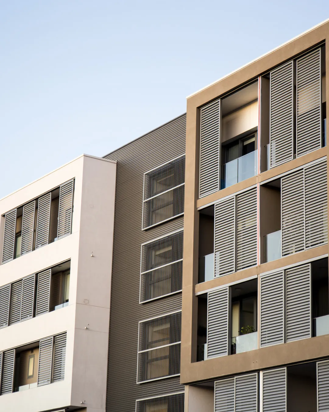 Modern apartment building facade with beige and white sections and horizontal window shutters.