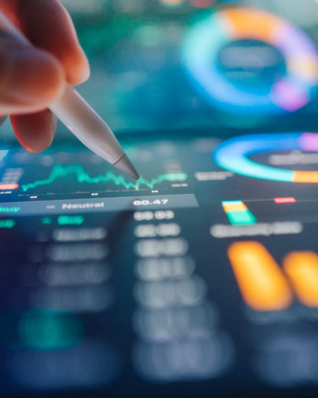 Hand holding a stylus pointing at a financial chart on a digital screen with graphs and data.
