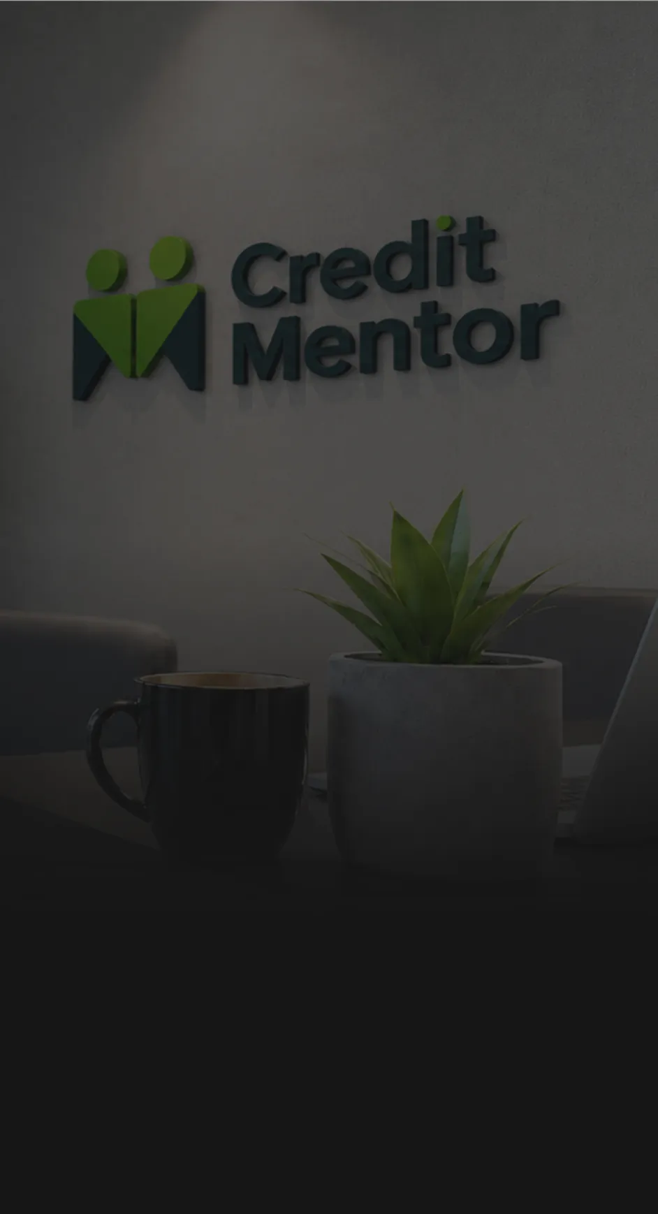 Лого на Credit Mentor на сива стена над черна чаша и саксия с растение на бюро.