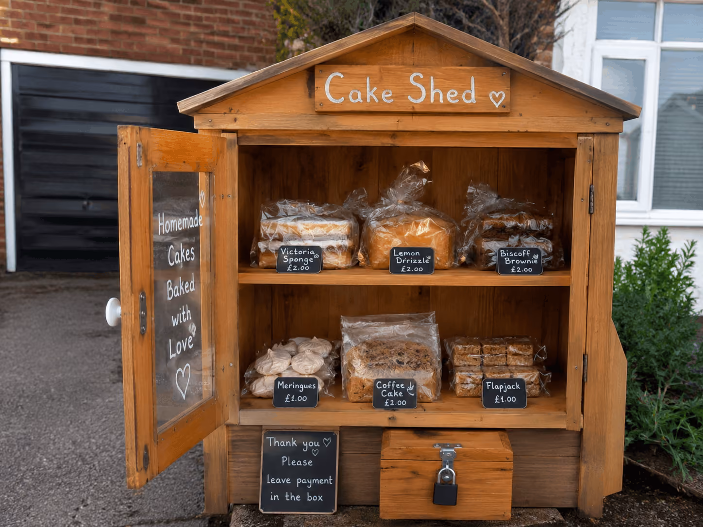 Wooden roadside cake shed with homemade cakes and signs asking to leave payment in the box.