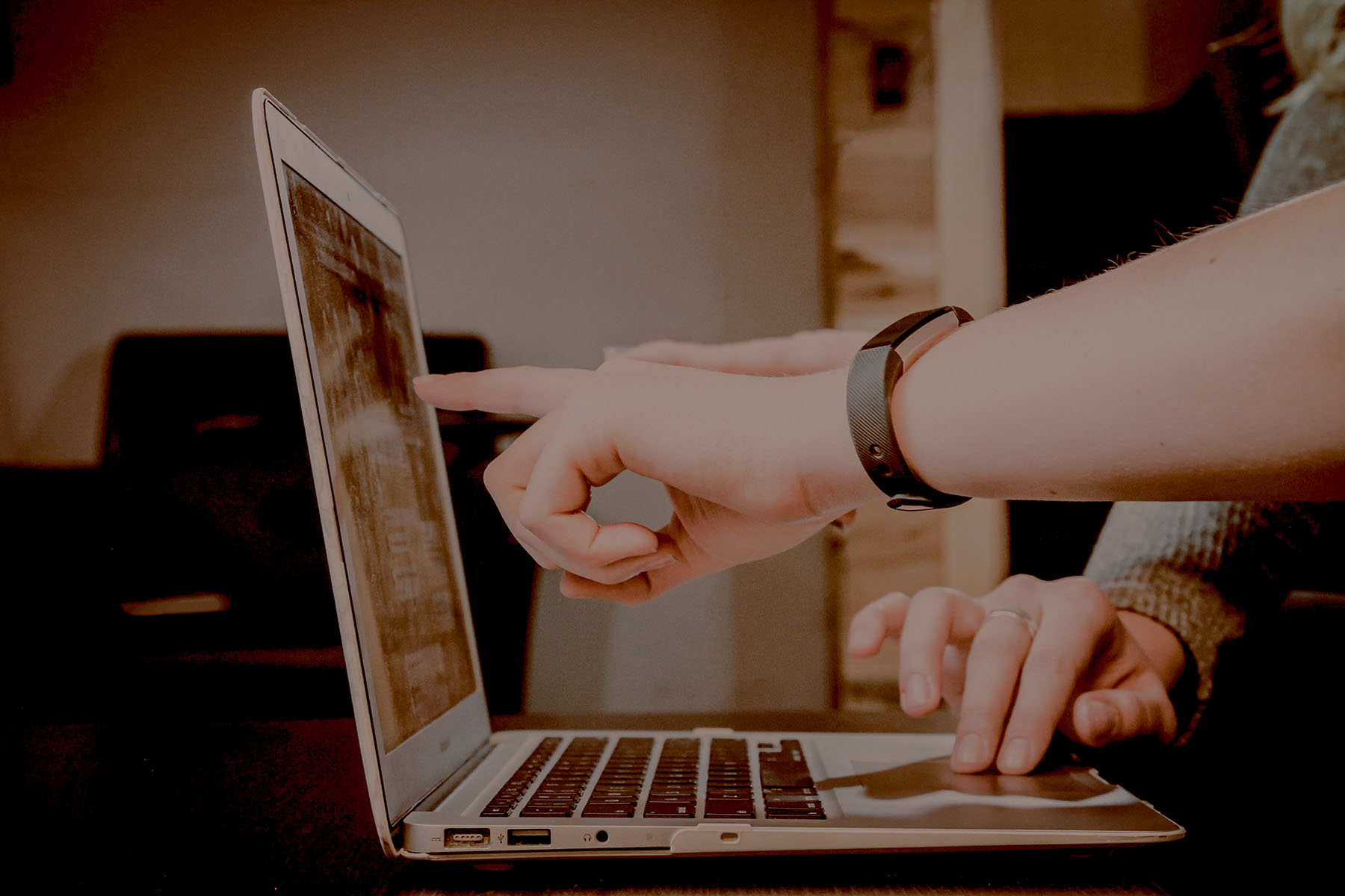 Person pointing at a laptop screen while another types on the keyboard.