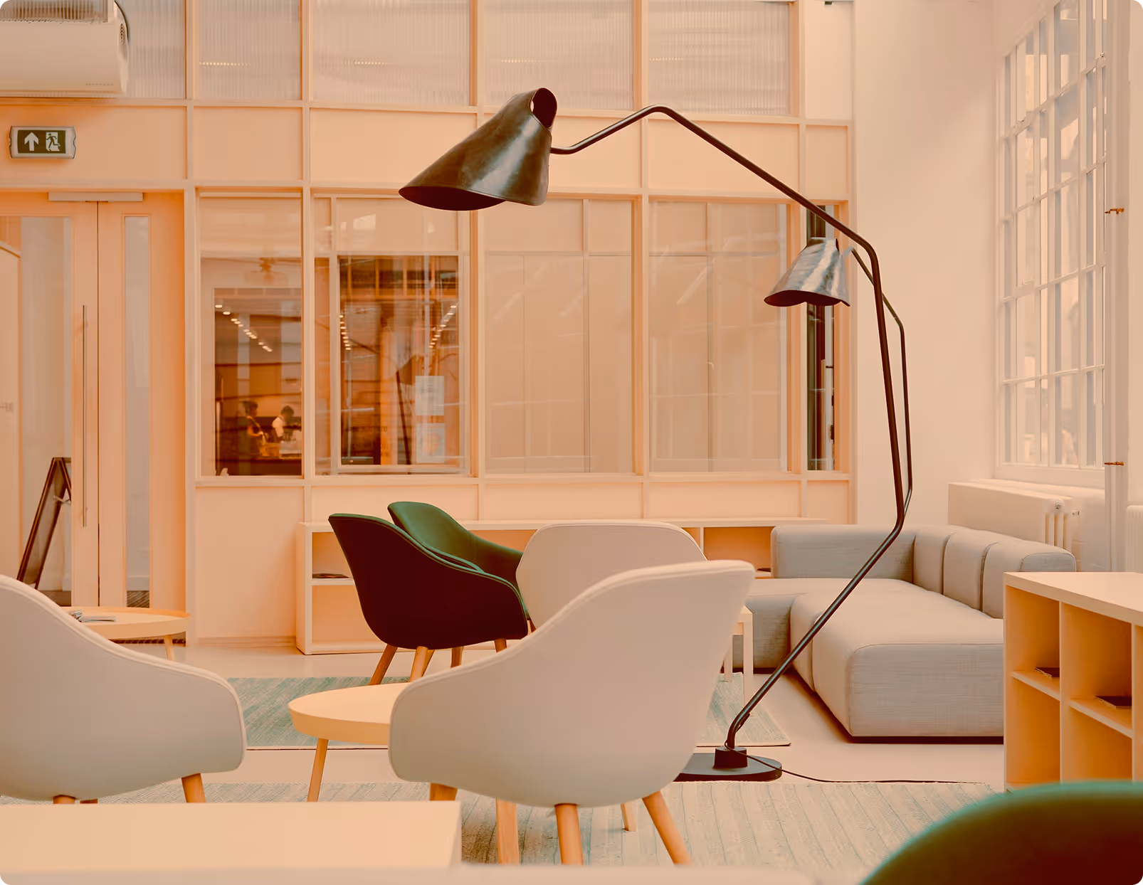 Modern lounge area with gray sofa, green and beige armchairs, round wooden tables, and tall black floor lamp.