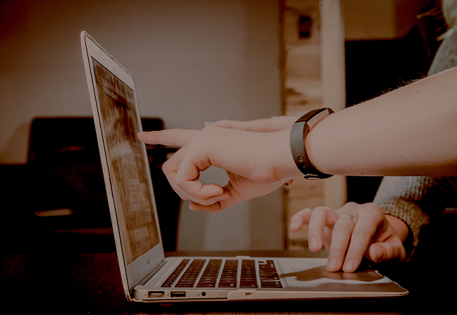 Close-up of two people using a laptop, one pointing at the screen while the other types.