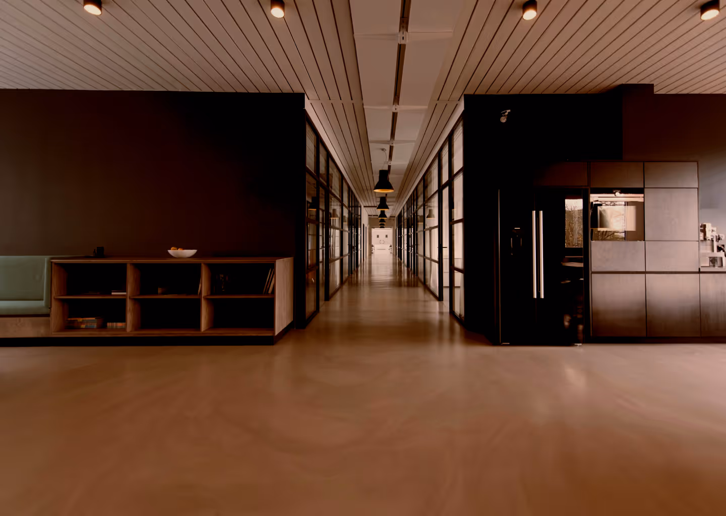 Long modern office hallway with glass-walled offices, wooden shelves, and overhead lighting.