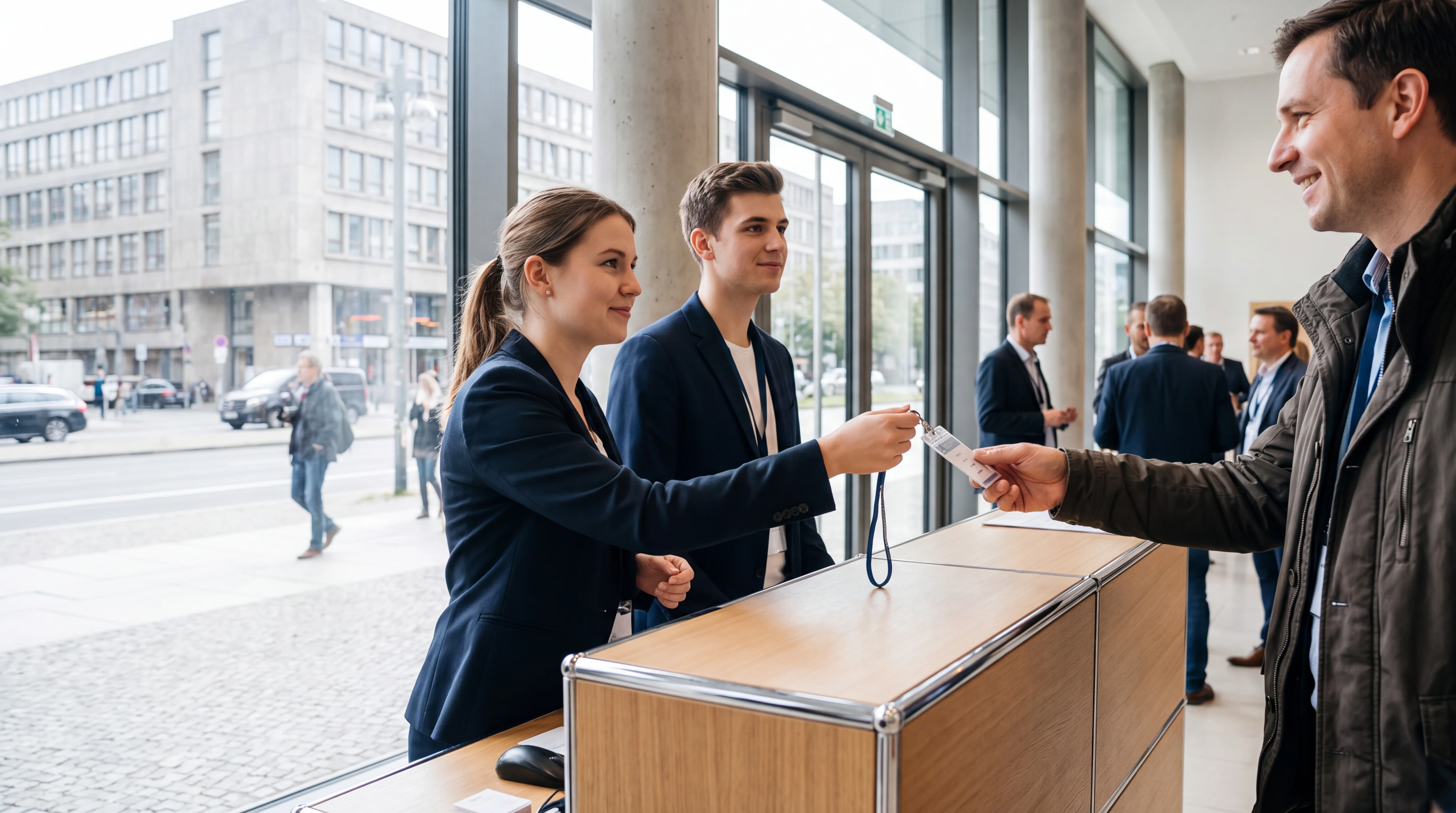 Eventpersonal in Berlin: zwei Hosts am Empfangstresen übergeben einem Gast den Badge, dahinter Glasfassade und Straße