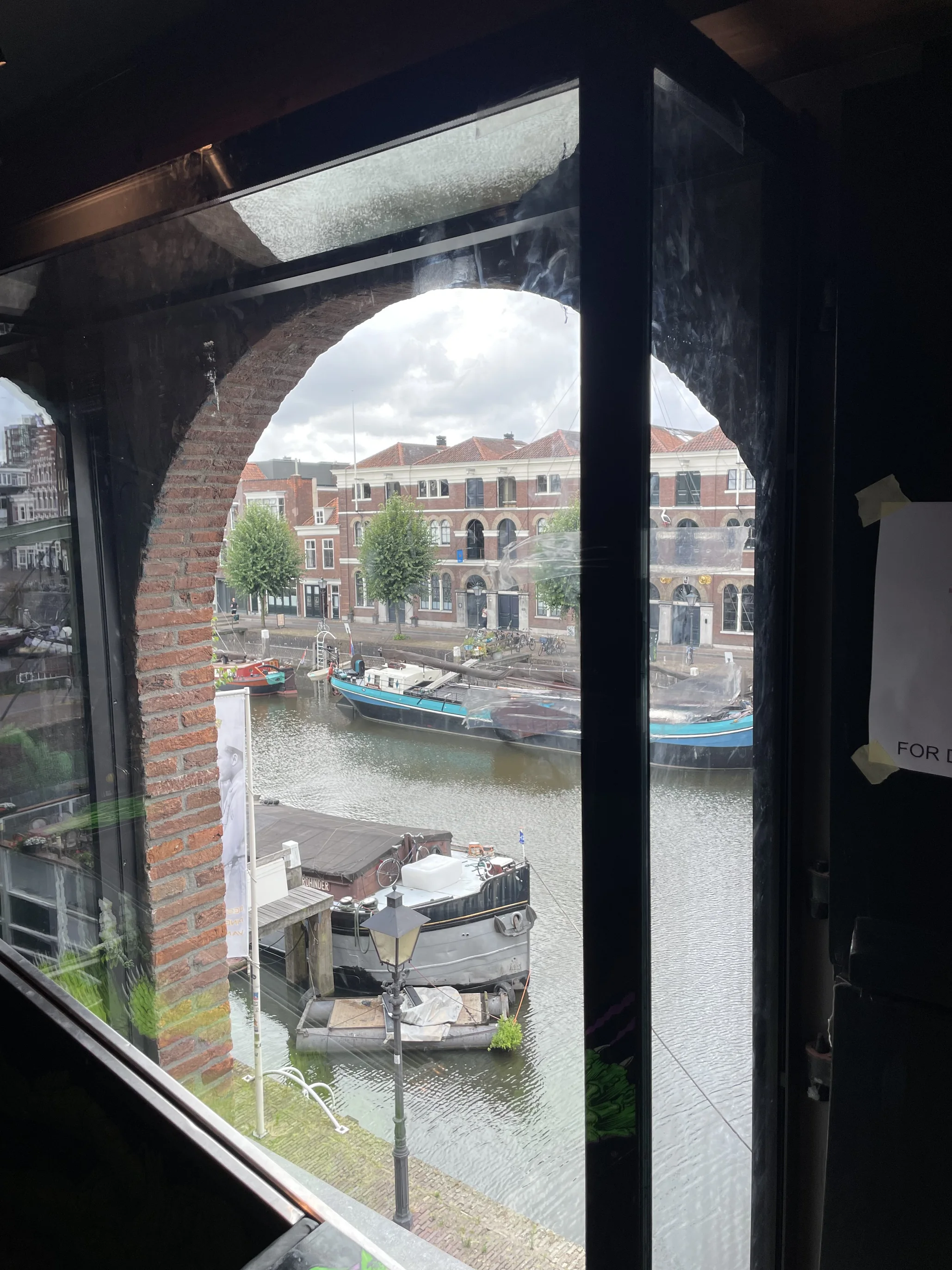 Uitzicht door een glazen etalage op het water en de historische bebouwing van Delfshaven.
