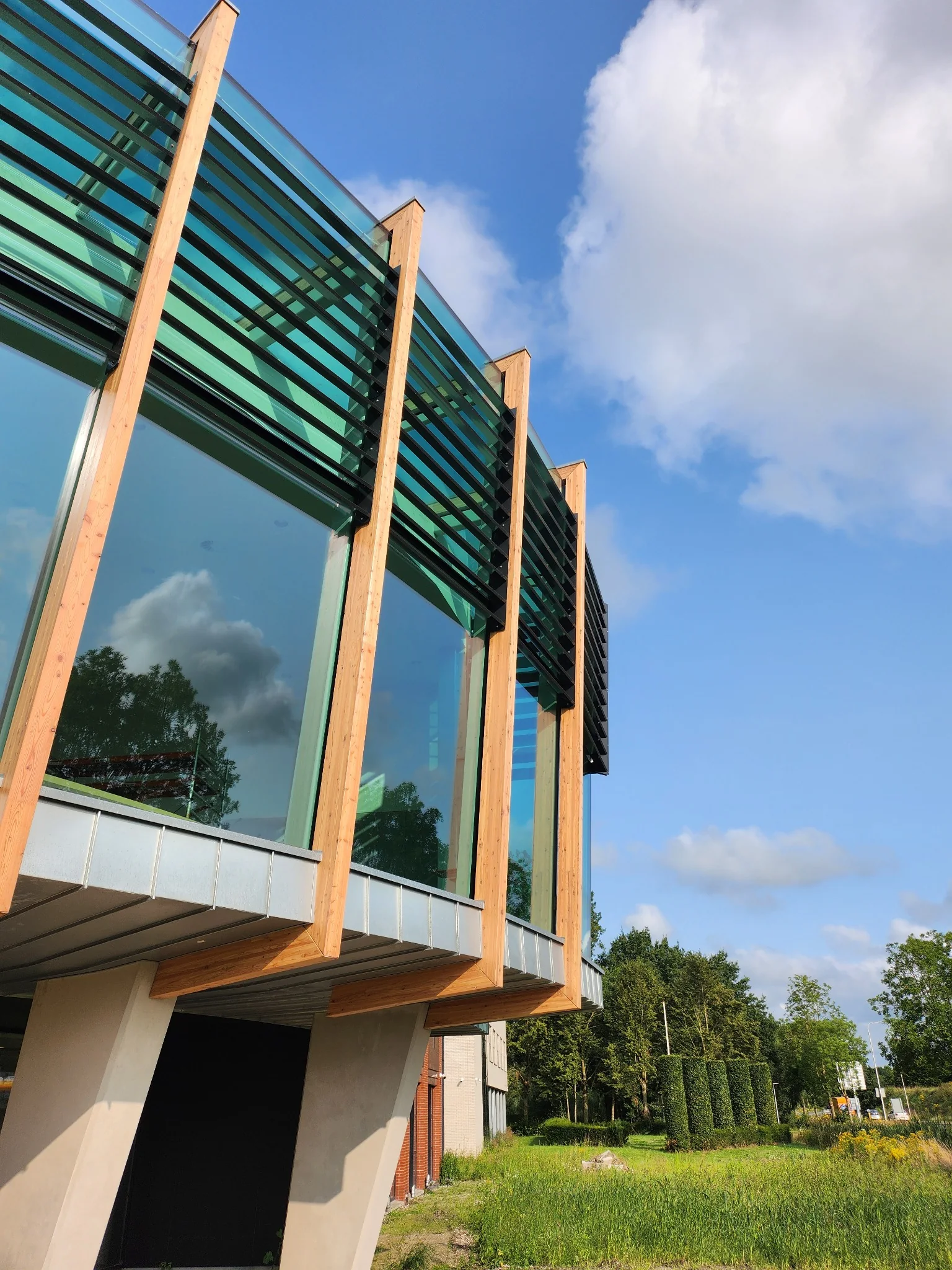 Detail van de vooroverhellende glasgevel met houten stijlen en horizontale lamellen.