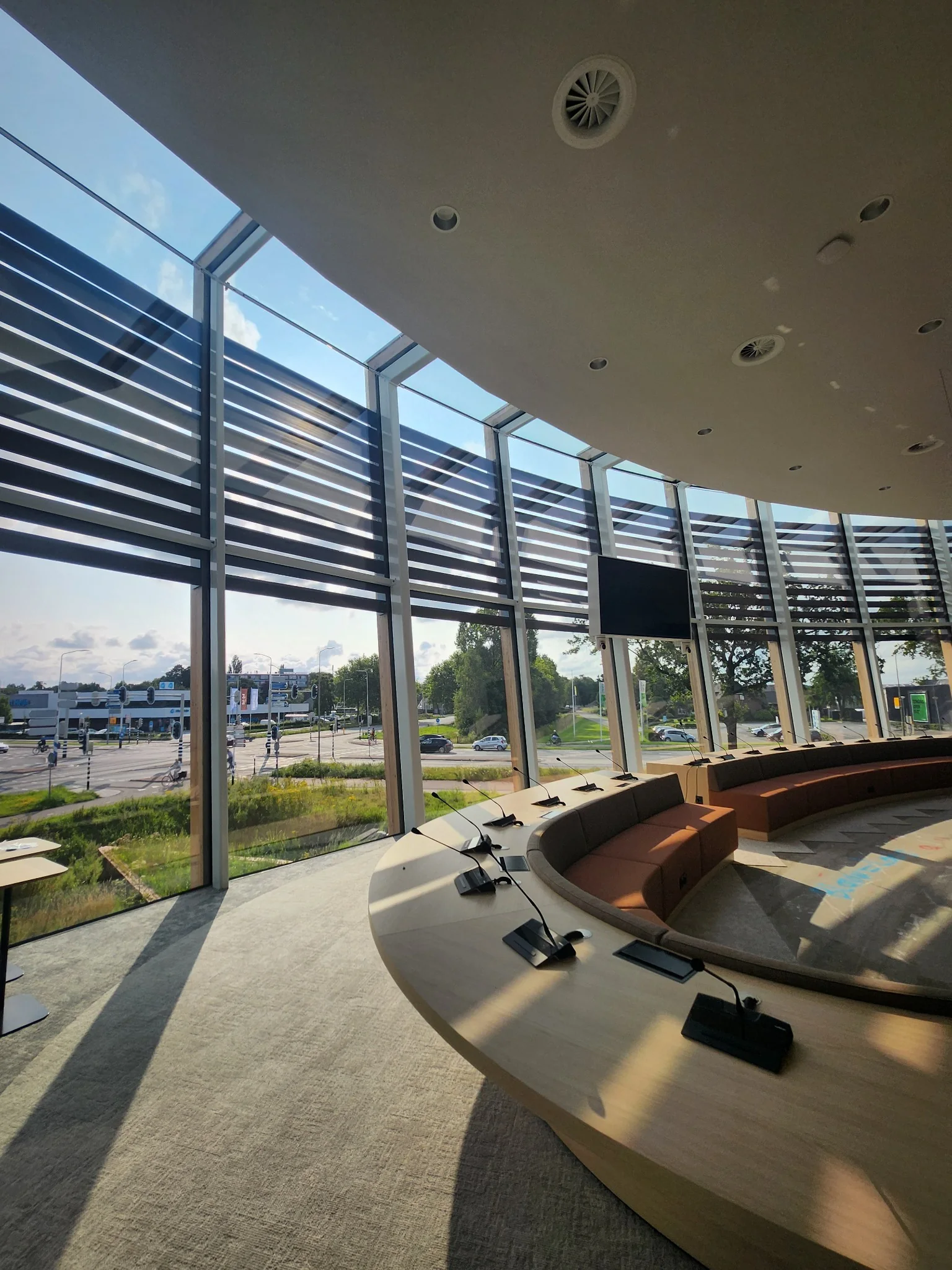 Interieur van de nieuwe raadzaal met gebogen opstelling en transparante gevel.