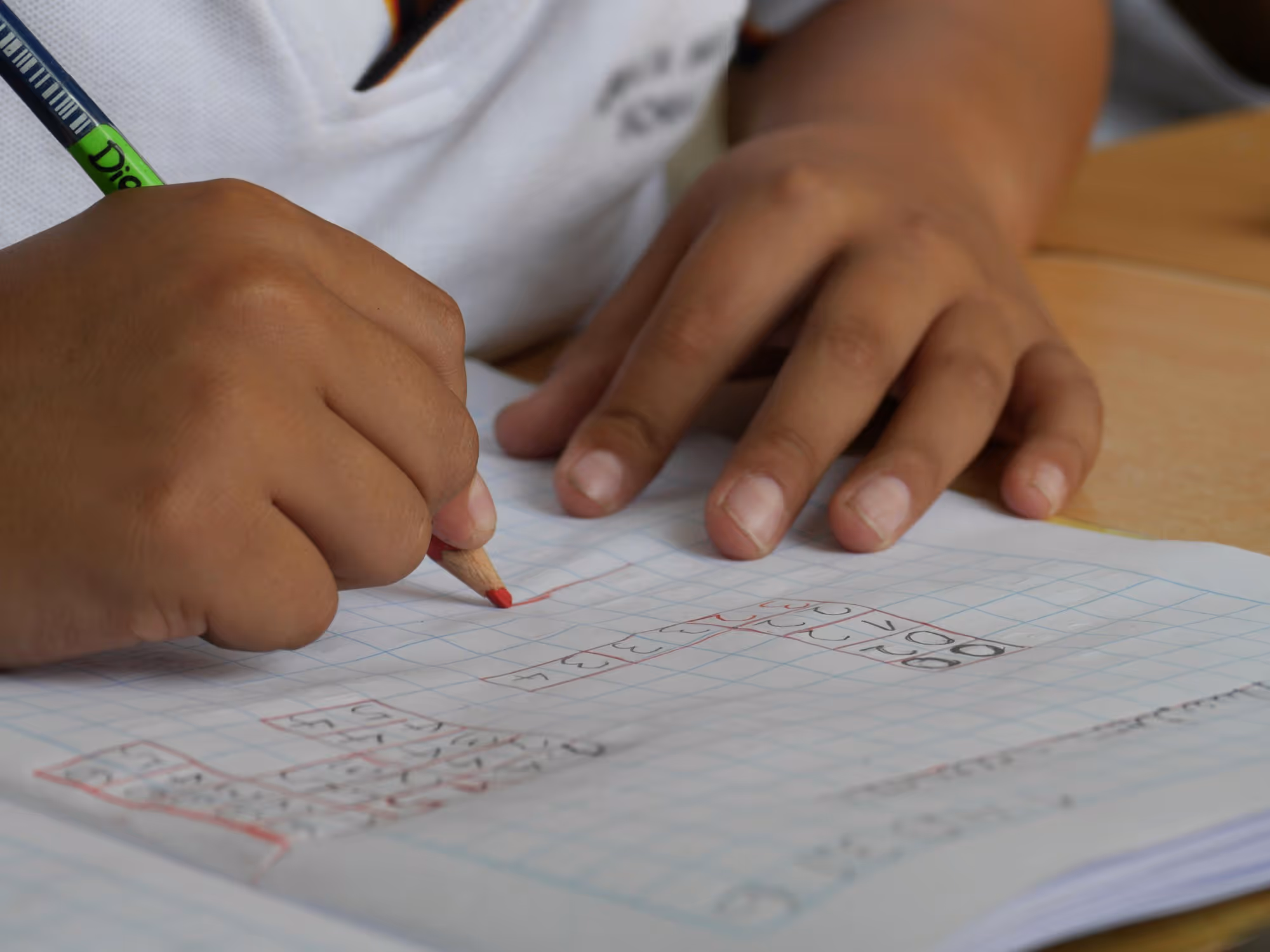 Child's hands holding a pencil and coloring on graph paper with numbers and grids.