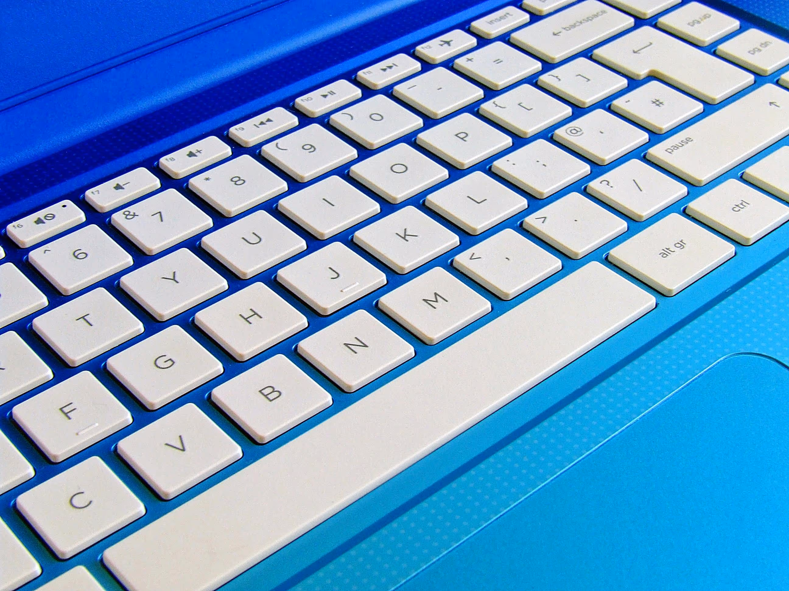Close-up of white keys on a blue laptop keyboard showing letters, numbers, and function keys.