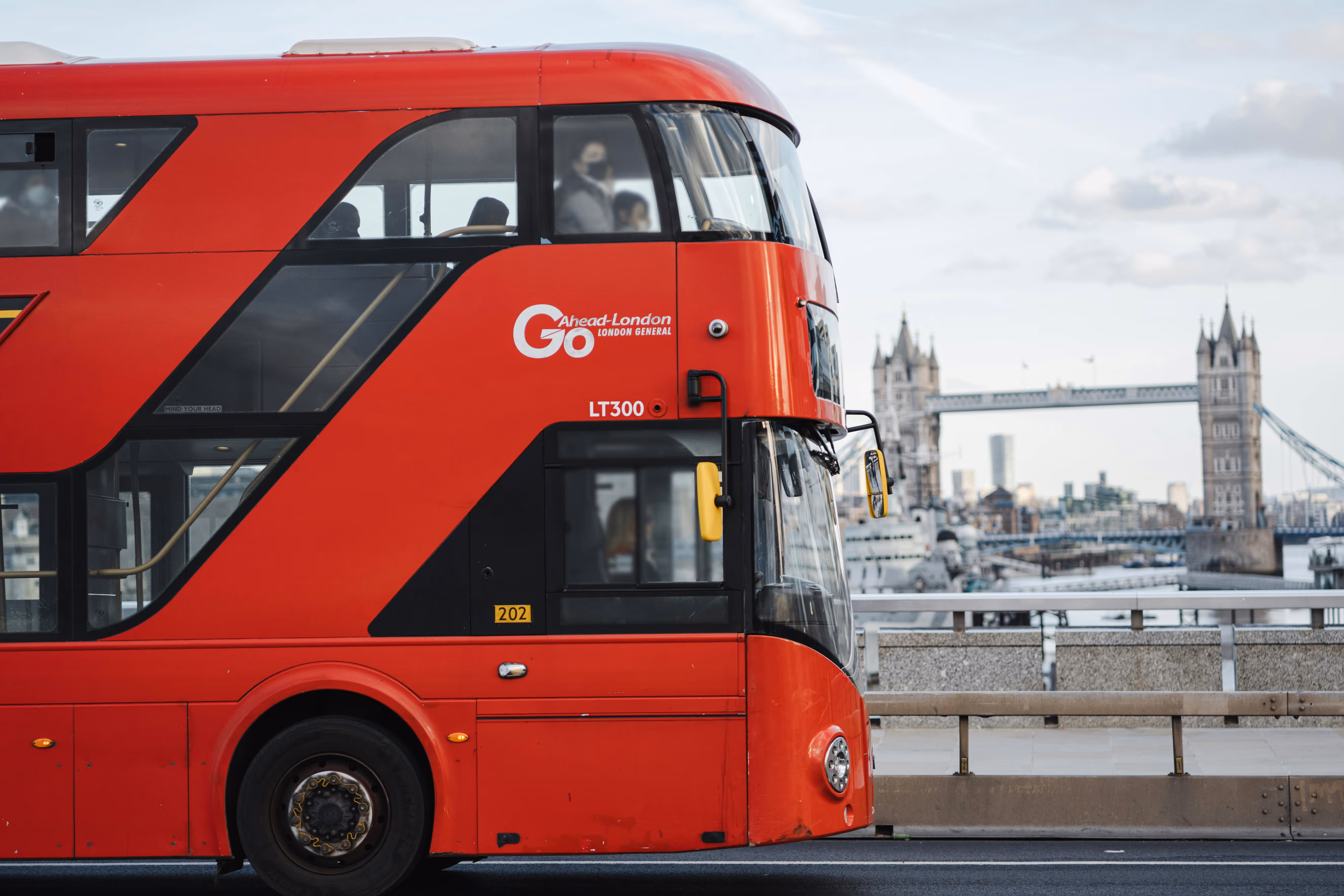 Side view of a red double-decker London bus with Tower Bridge in the background.