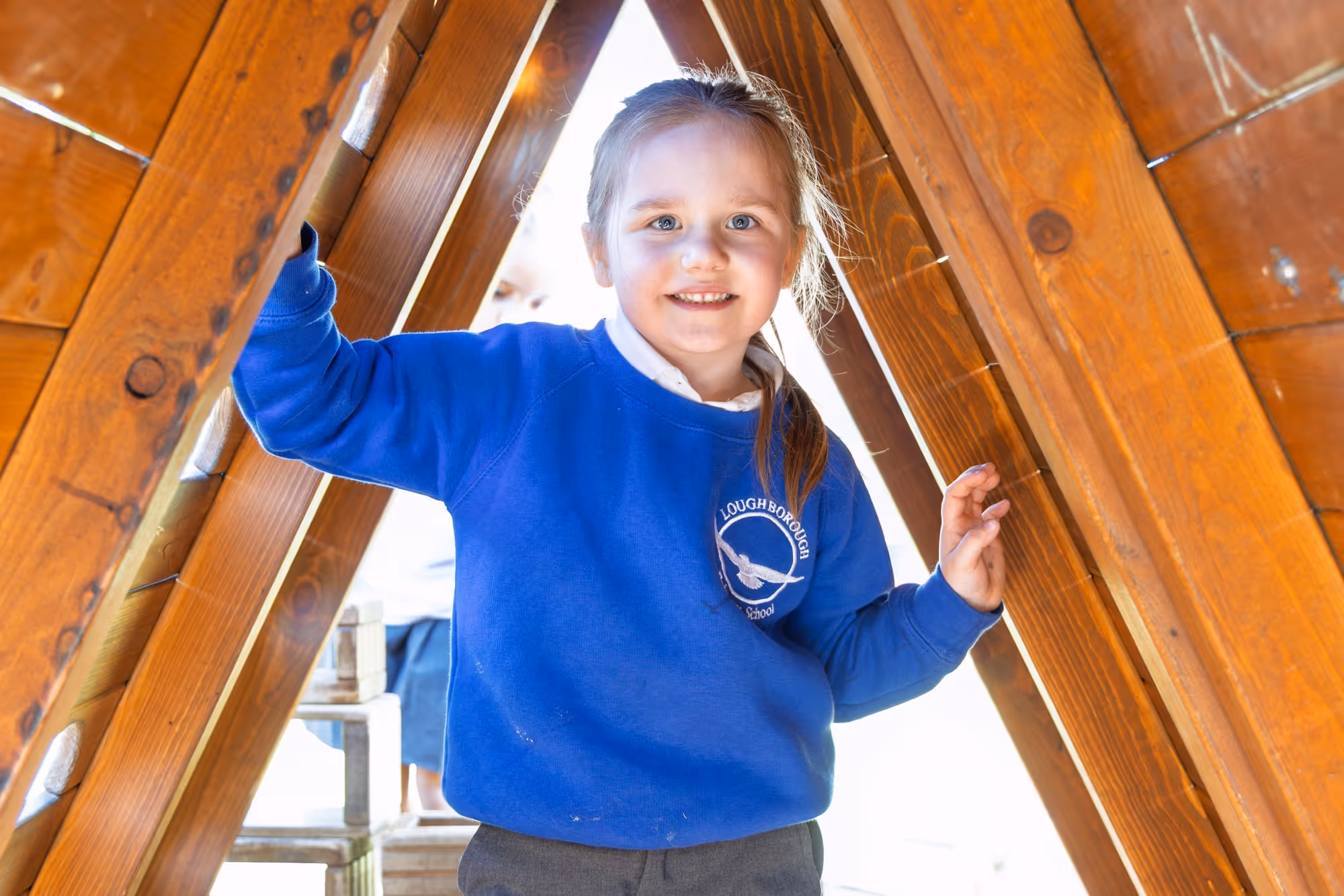 Smiling girl in a blue Loughborough school sweatshirt standing inside a wooden triangular structure.