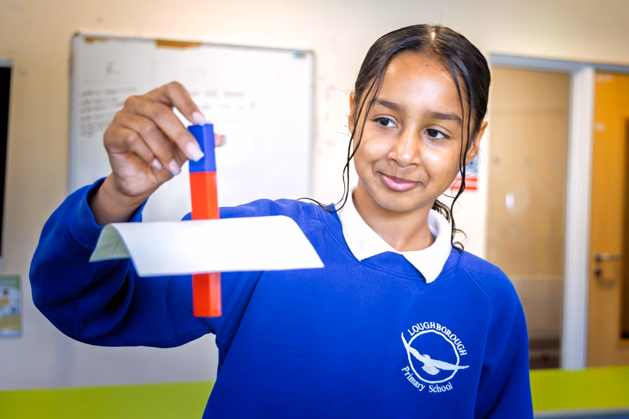 Girl from Loughborough Primary School holding a red and blue magnet with a white paper attached.