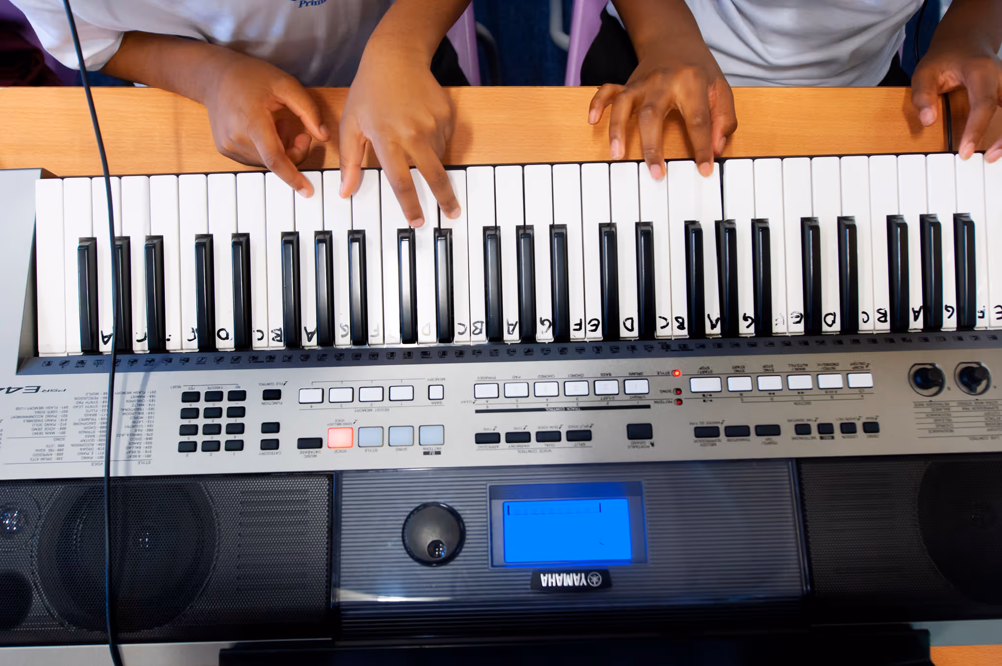 Three people playing a Yamaha keyboard with labeled piano keys and one key lit red.