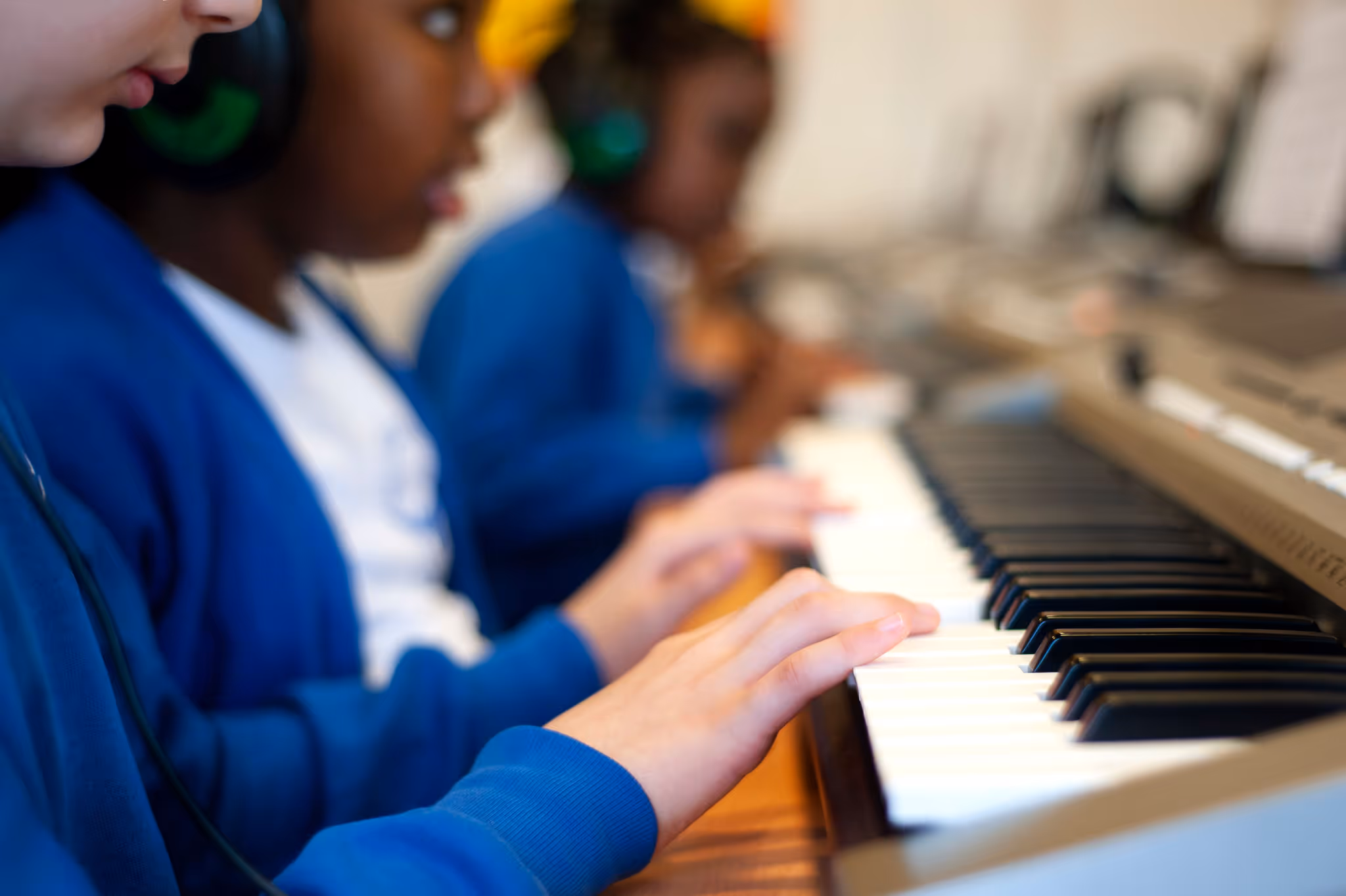 Children wearing headphones and blue uniforms playing an electronic keyboard in a music class.