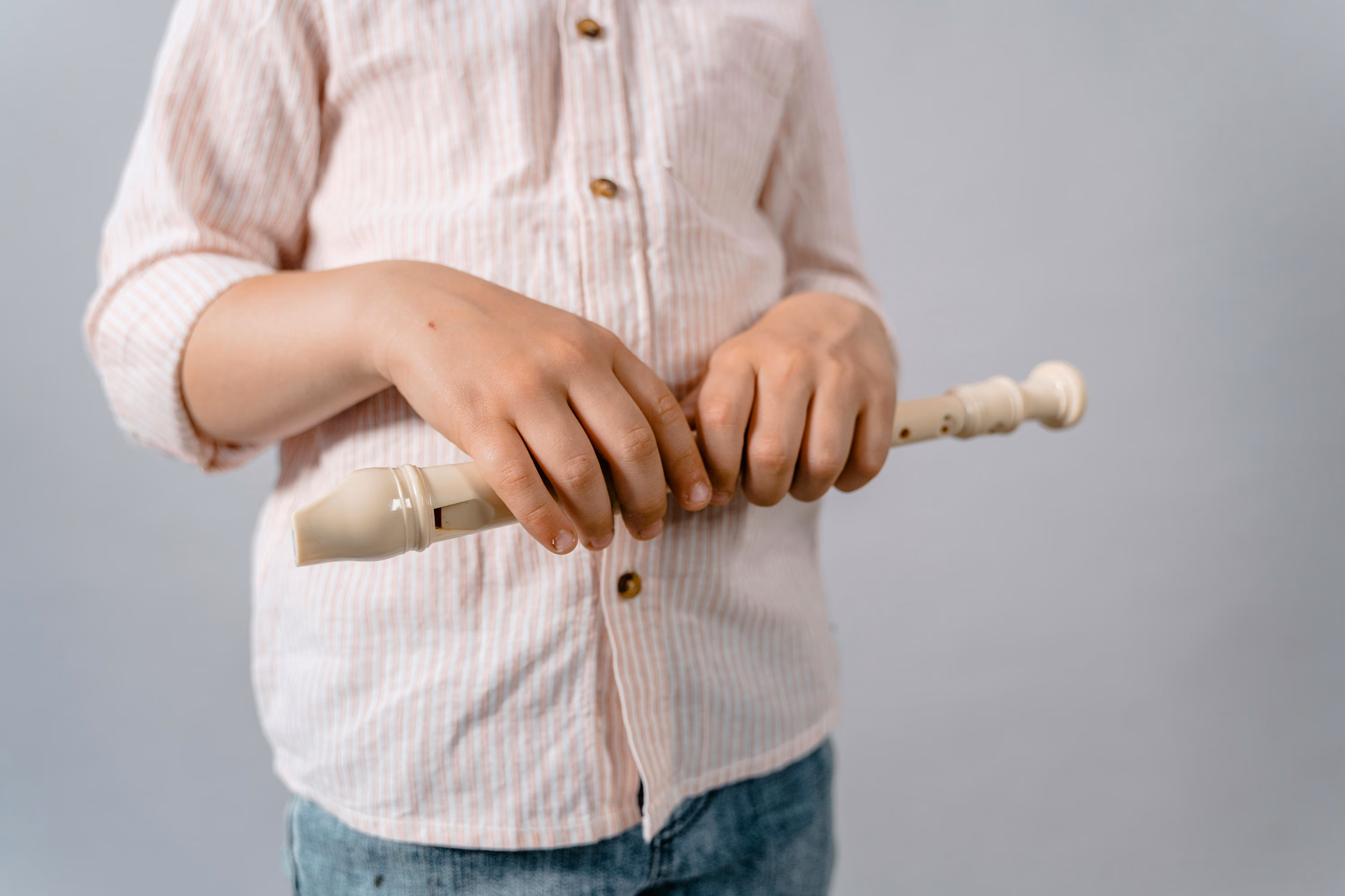 Child in striped shirt holding a white recorder musical instrument with both hands.